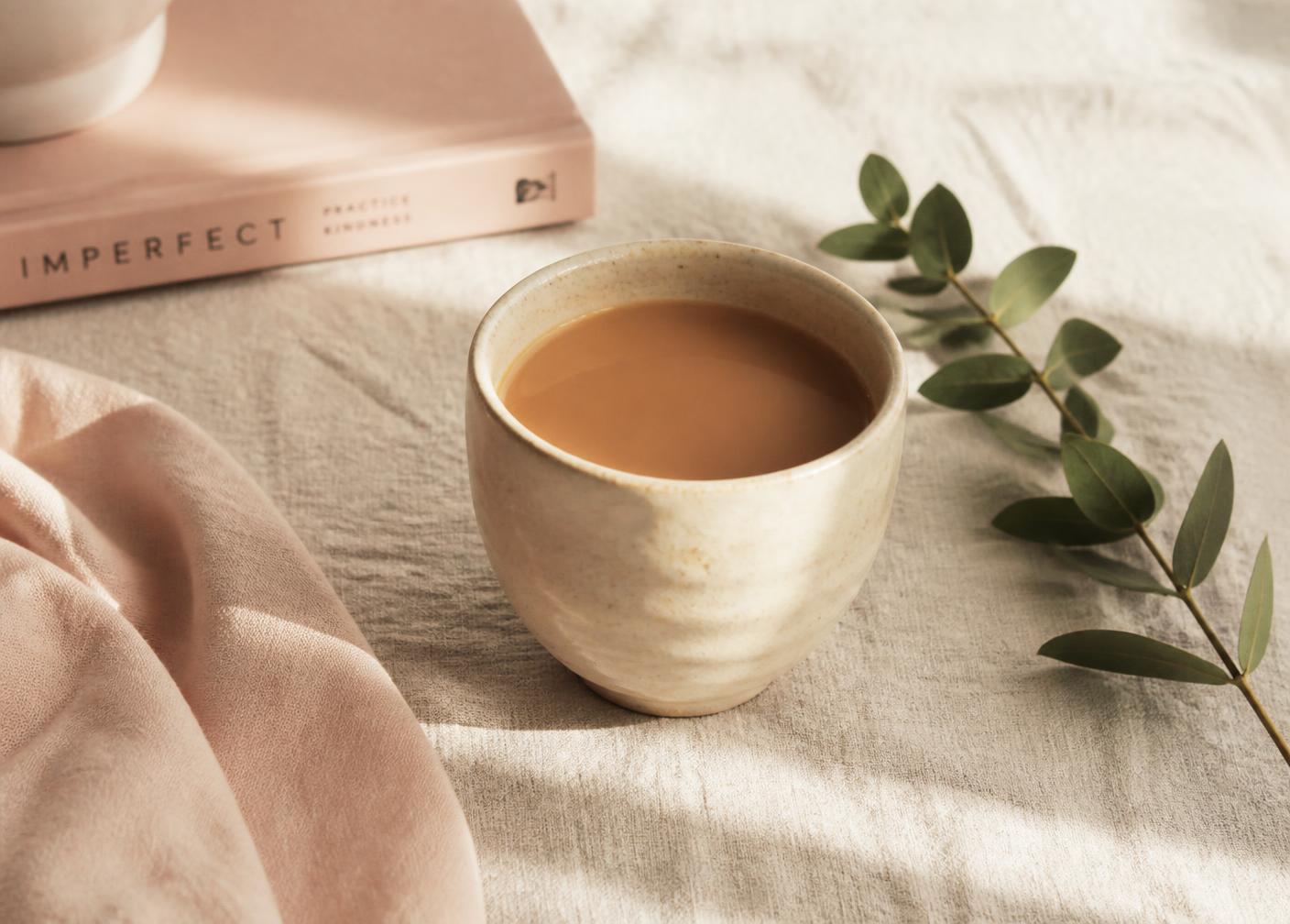 A handmade ceramic cup of chai on cream linen beside a sprig of leaves